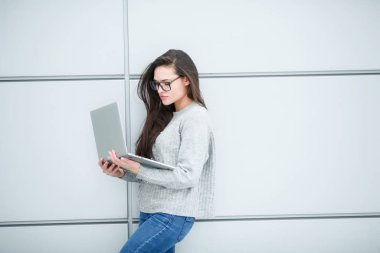 Genç bir kadın programcı elinde dizüstü bilgisayarla tek renkli bir arka planda duruyor.