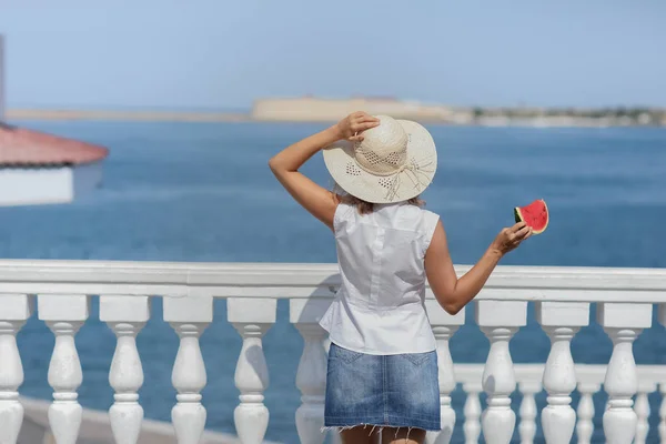 Volwassen vrouw op de achtergrond van de zee met een plak watermeloen terug naar de camera — Stockfoto