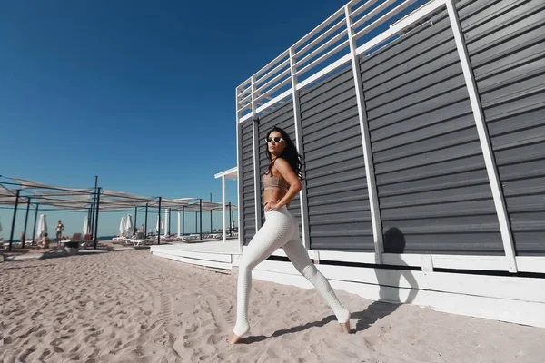 Genç ve güzel fitness kızının fotoğrafı arka planda deniz kıyısı ile spor egzersizleri yapıyor. — Stok fotoğraf