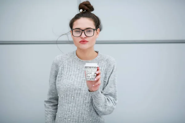 Una mujer con vasos bebiendo café contra una pared gris —  Fotos de Stock