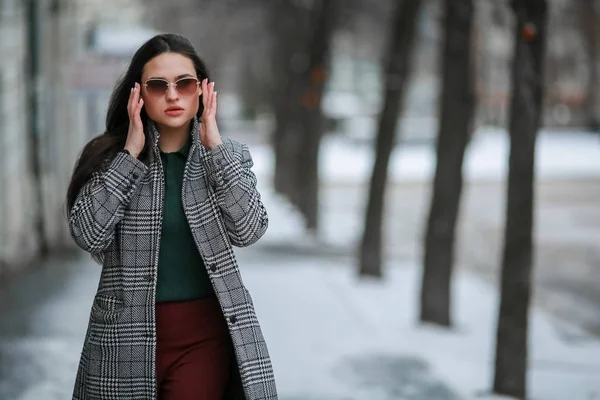 Egy nő kabátban és napszemüvegben télen a városban sétál. — Stock Fotó