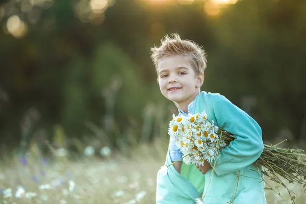 Chlapec blond dítě zblízka s kyticí sedmikrásek v rukou na rozmazaném pozadí venku — Stock fotografie