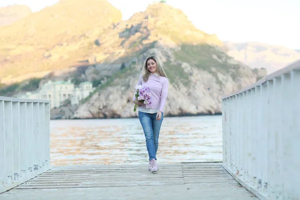 Een vrouw in volle gestalte staand op een houten pier op de achtergrond van bergen — Stockfoto