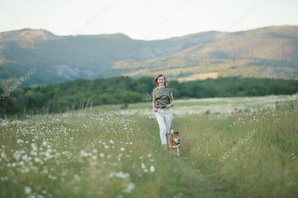 A dog and a woman running through a field of green grass
