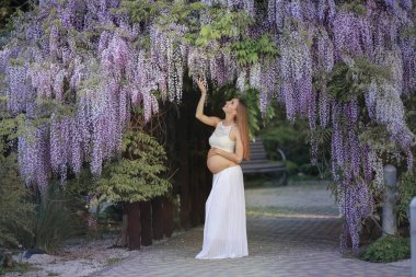 Çiçekli Wisteria bahçesinde karnı açık hamile bir genç kadın.