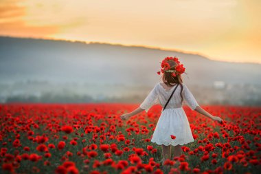 Kızıl gelincik çelengi takmış tarlada bir kadın.