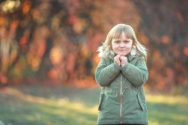 Neşeli bir çocuk sonbaharda ağaçlarla kaplı bir bahçede yürür.