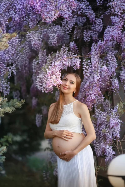 Belle femme enceinte aux cheveux longs au printemps dans le jardin avec des arbres en fleurs — Photo