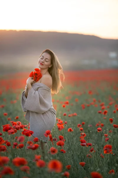 Una hermosa mujer con hombros desnudos y un suéter largo en un campo con amapolas —  Fotos de Stock