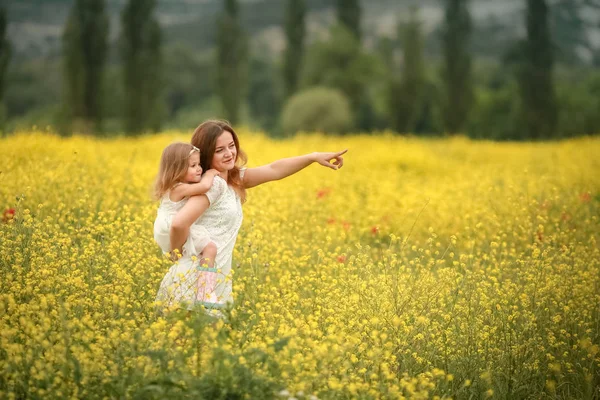 Gelukkige familie zomervakantie. Moeder met meisje in verkrachtingsveld genietend van het leven bij zonsondergang. Mooie brunette met lang gezond haar. Zorgeloos meisje boven geel veld en blauwe lucht. Landelijk landschap. — Stockfoto