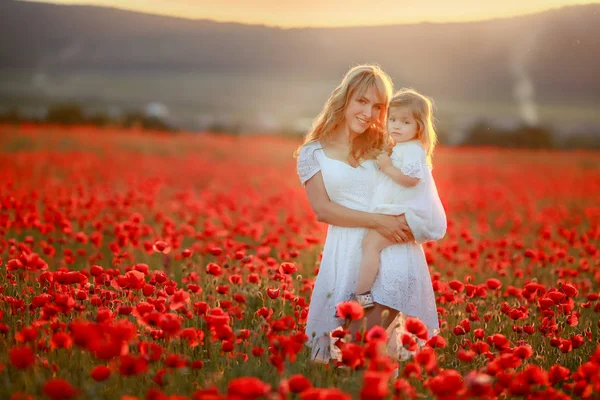 Daughter child 3 years and a beautiful mother in white dresses in a field with red flowers — Stock Photo, Image