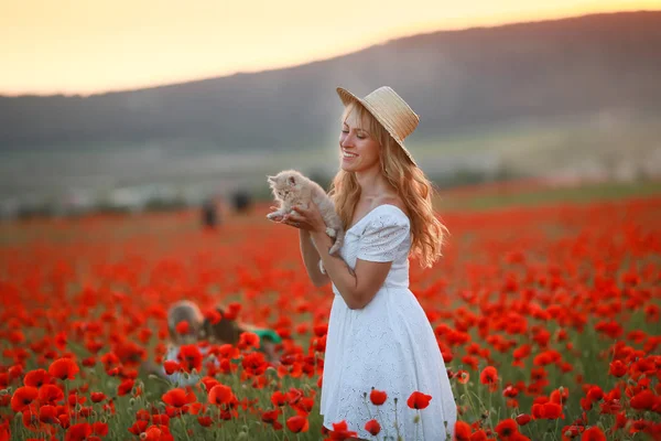 Una hermosa mujer en un sombrero de paja en un campo agrícola con amapolas —  Fotos de Stock