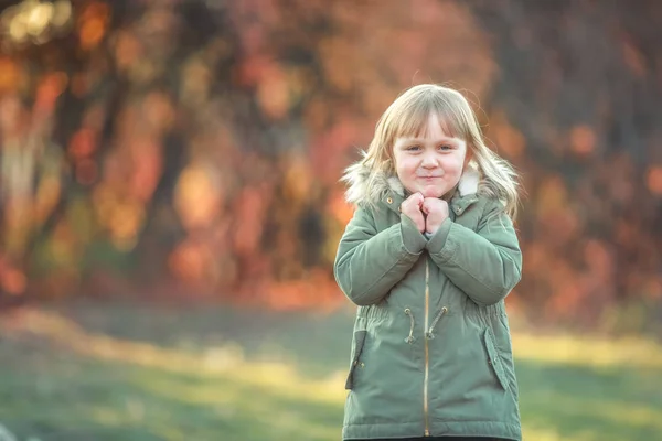 Ein fröhliches Kind spaziert im Herbst durch einen Garten mit Bäumen, die mit einem gelben Blatt bedeckt sind — Stockfoto