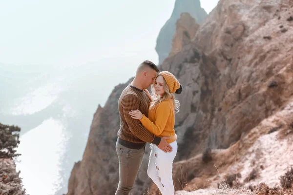 Молодой сильный мужчина обнимает свою возлюбленную женщину на вершине горы на фоне каменных гор — стоковое фото