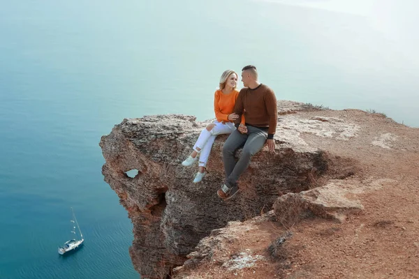 Een man en een vrouw zitten op een rots met hun benen over kliffen. — Stockfoto