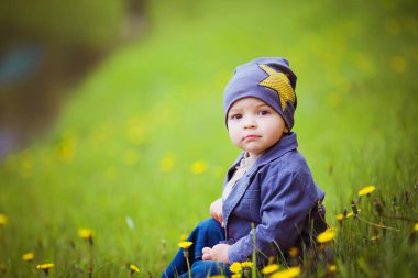 Mutlu bebek güneşli bir bahar gününde yeşil bir çayırda oturuyor sarı karahindibaların açtığı