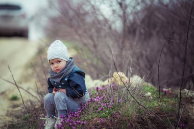 4-5 yaşlarında, orman yolunda gri şapkalı bir çocuk.