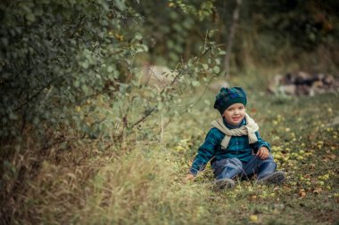 Kauçuk botlar ve sonbahar kıyafetleri içinde ormanda yürüyen 5-7 yaşında bir çocuk.