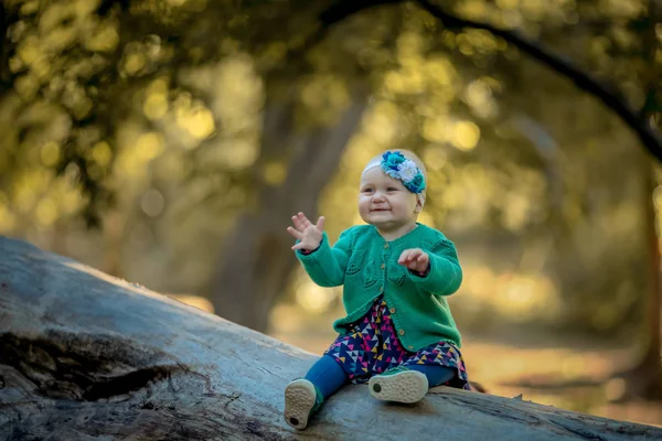 Baby girl sitting on a log and smiling enjoying life — Stock fotografie