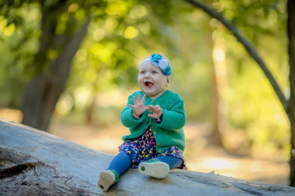 Baby girl sitting on a log and smiling enjoying life — Stock fotografie