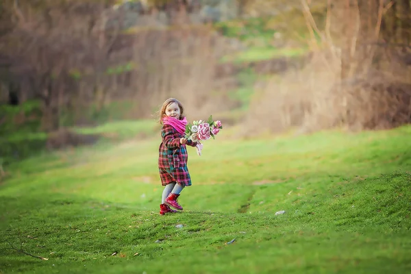 7-8 yıl ceketli bir kız baharın başında yeşil bir çayırda yürür. — Stok fotoğraf