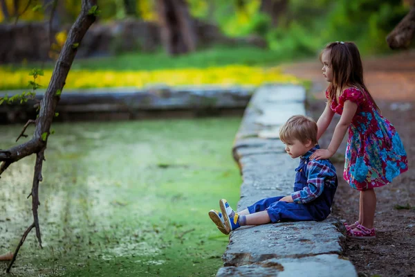 Niños un niño y una niña se sientan en el borde de un lago bosque artificial —  Fotos de Stock