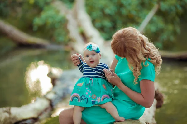 Een gezin van twee personen moeder en dochter baby zitten in de natuur bij meren en tussen bomen — Stockfoto