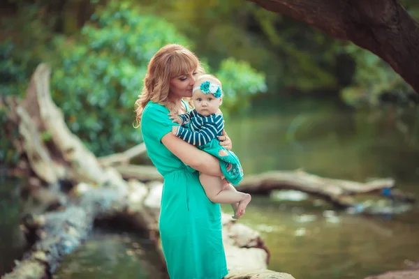 İki kişilik bir aile anne ve kız bebek göl kenarında ve ağaçların arasında oturuyor. — Stok fotoğraf