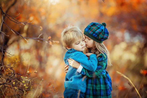 Niños vestidos con ropa cálida de otoño abrazan y sonríen en el bosque rojo y amarillo — Foto de Stock