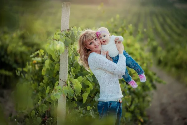 Lycklig kvinna mamma leker med barnet i armarna i rader av jordbruksdruvor — Stockfoto