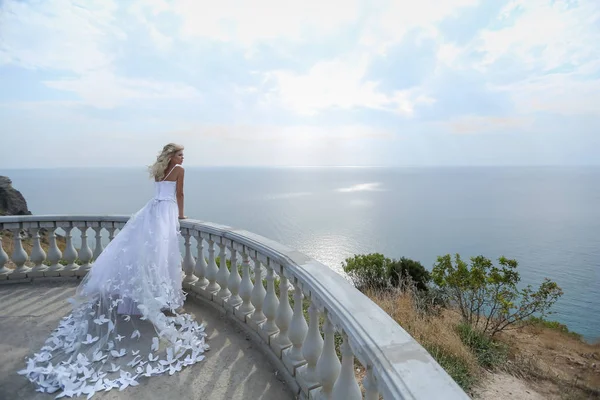 Μια νύφη με ένα όμορφο λευκό νυφικό στέκεται σε ένα μπαλκόνι στην κορυφή ενός βουνού σε μια ηλιόλουστη μέρα του καλοκαιριού — Φωτογραφία Αρχείου