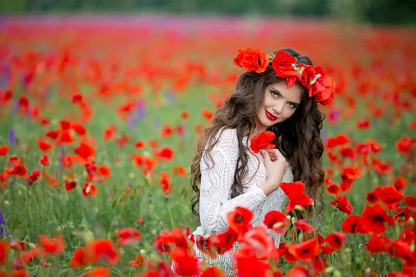 Vrolijk meisje in een veld met rode klaprozen in een natuurlijk veld met bloemen — Stockfoto