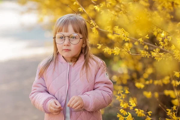 Dívka v růžovém plášti sbírá žluté listy v parku na podzim — Stock fotografie