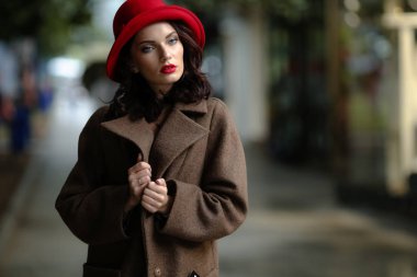 28-30 yaşlarında, siyah saçlı, zarif ceketli ve kırmızı aksesuarlı bir kadın.