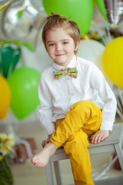 Güneşli bir günde, parlak bir odada balonların arka planında eğlenen bir çocuk.