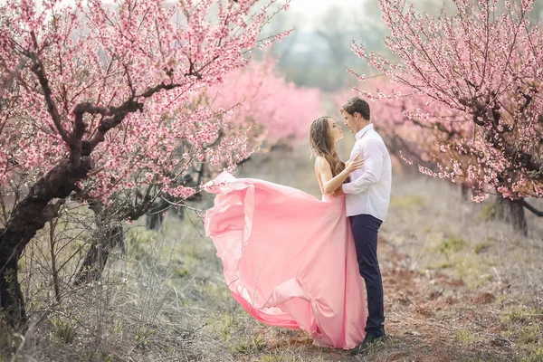 Romantische bruidegom bruid kussen op voorhoofd terwijl je tegen muur bedekt met roze bloemen — Stockfoto