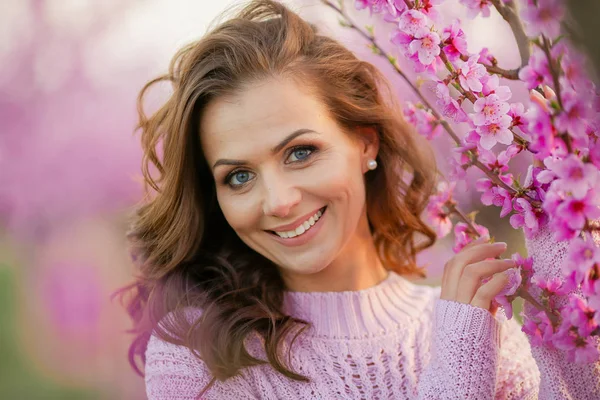 桜の花が咲く庭の背景にあるセーターの中に巻き毛の美しい大人の女性 — ストック写真