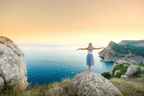 Egy fiatal turista lány ruhában csodálja a tájat a hegy tetejétől a tengerig. — Stock Fotó