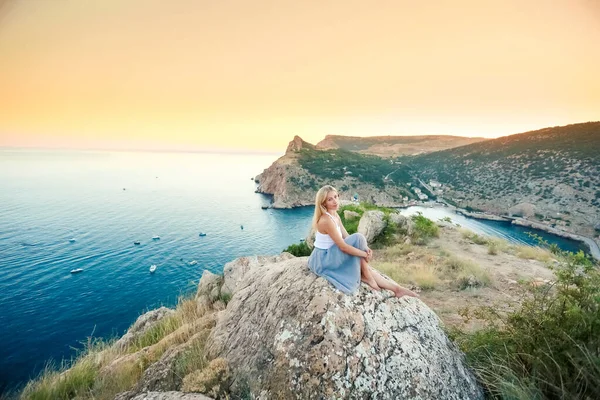 若い美しい女性は海の湾の上の山の岩の上に座っている — ストック写真