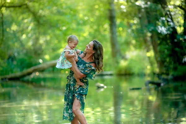 Mamá con su hija pequeña en un paseo de verano cerca del agua en el bosque — Foto de Stock