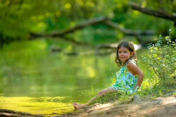 Ragazza 4-5 anni in abito verde e a piedi nudi sullo sfondo del fiume nel bosco — Foto Stock