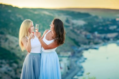 İki mutlu genç kadın birlikte içiyor ve bir dağın tepesinde eğleniyorlar.