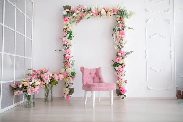 Cenário na sala branca. Arco de flores e uma poltrona rosa com um buquê de flores — Fotografia de Stock