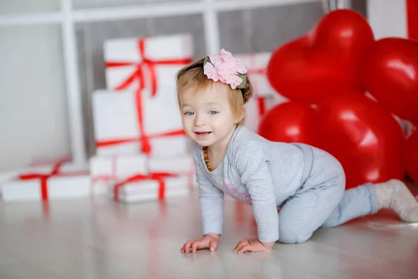 Bebê menina rastejando de joelhos em uma sala brilhante no fundo sobre o fundo de balões e caixas brancas — Fotografia de Stock