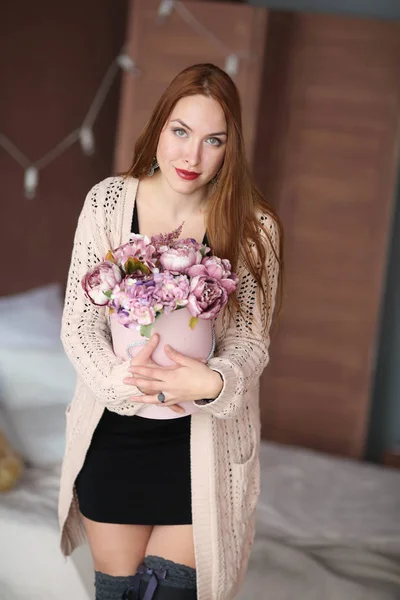 長い赤い髪の美しい女性と彼女の手の中にバスケットの花と暖かいピンクのセーター — ストック写真