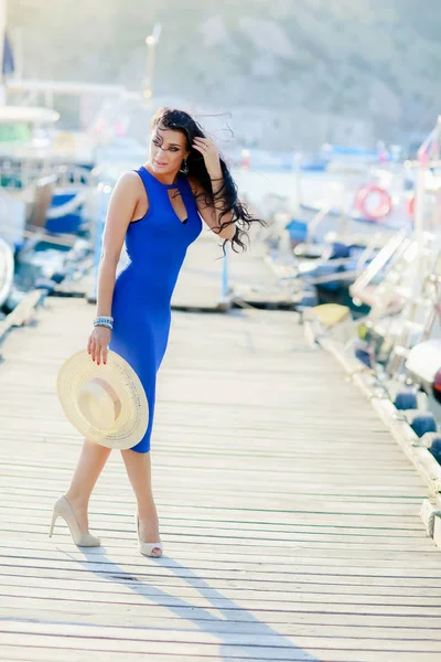 Piękna kobieta w niebieskiej sukience kobieta wiruje na drewnianym przystani łodzi i trzyma biały kapelusz w rękach — Zdjęcie stockowe