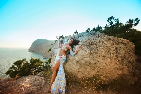 Uma mulher em um vestido oriental está em uma rocha com as costas contra uma rocha — Fotografia de Stock