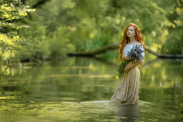 Eine Frau im Kleid und mit einem Strauß in der Hand steht am See im Wald — Stockfoto