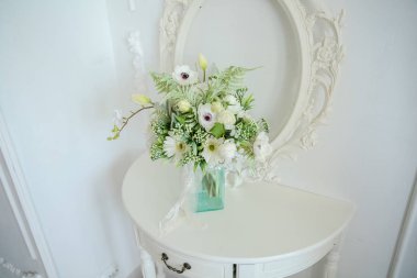 Masada bir vazo çiçek olan beyaz bir duvara karşı bir Versailles masası.