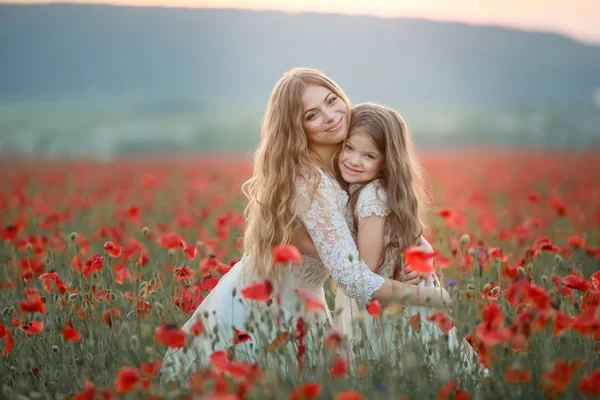 Молодая мама обнимает дочь в поле ярко-красными маками — стоковое фото